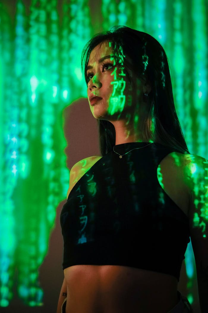 A woman in a dark room with green digital matrix code projected on her, evoking a sci-fi atmosphere.
